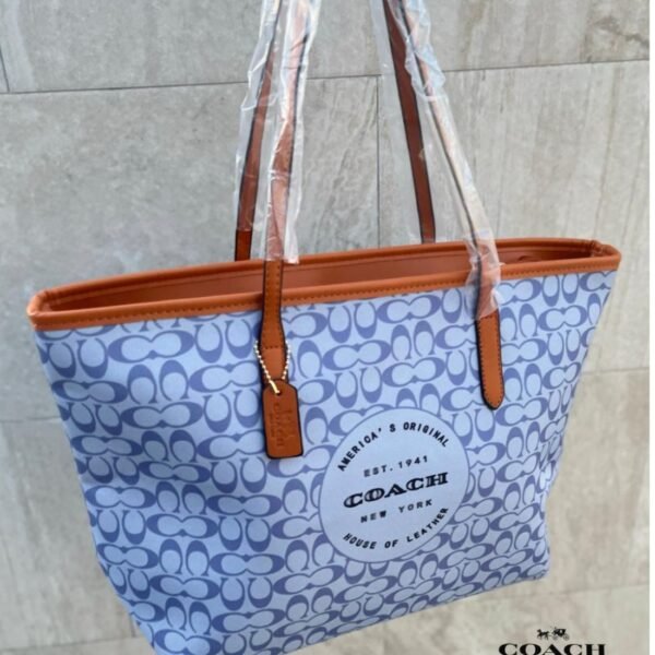 Cartera COACH tote color azul claro con detalles camel y logo circular.