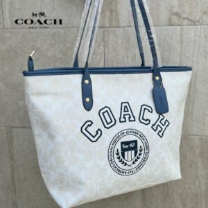 Cartera COACH tote color crema con detalles azul marino y logo bordado.