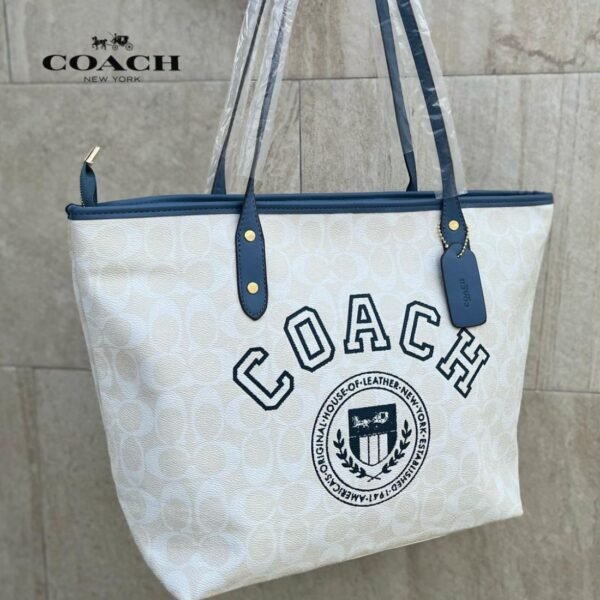Cartera COACH tote color crema con detalles azul marino y logo bordado.