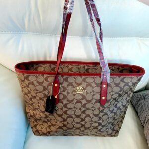 Cartera COACH tote marrón con borde vino tinto y logo dorado.