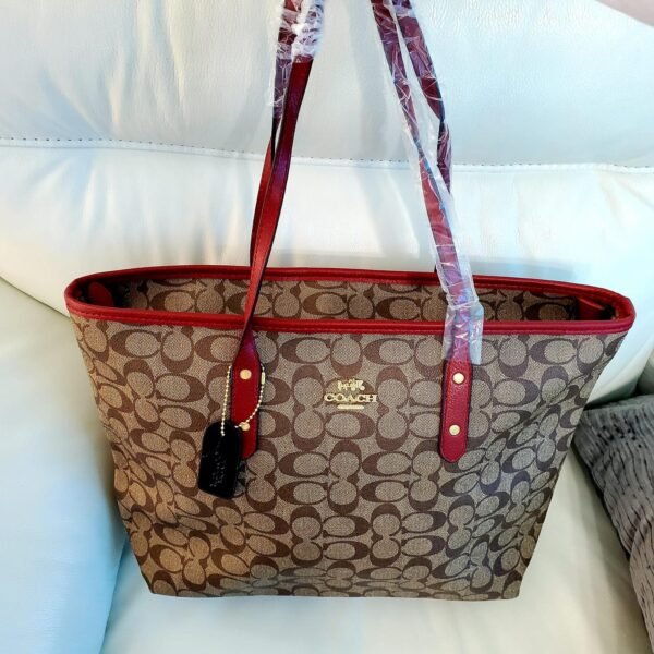Cartera COACH tote marrón con borde vino tinto y logo dorado.